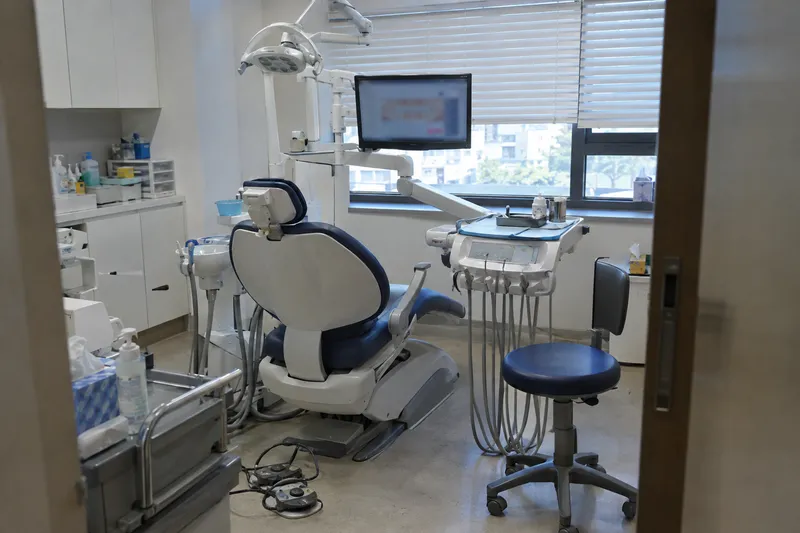 An empty dental treatment room with a reclined chair, overhead light, and a monitor beside the window (illustrative image)