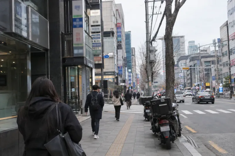 A busy street in Seoul's Gangnam district with pedestrians, storefronts, and parked motorcycles (illustrative image)